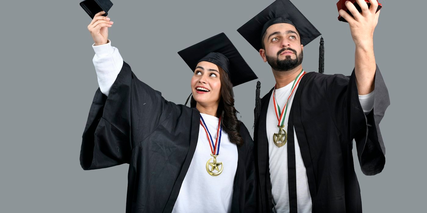 Un hombre y una mujer vestidos de graduación y sosteniendo un trofeo — Ayudas para deportistas y artistas jóvenes