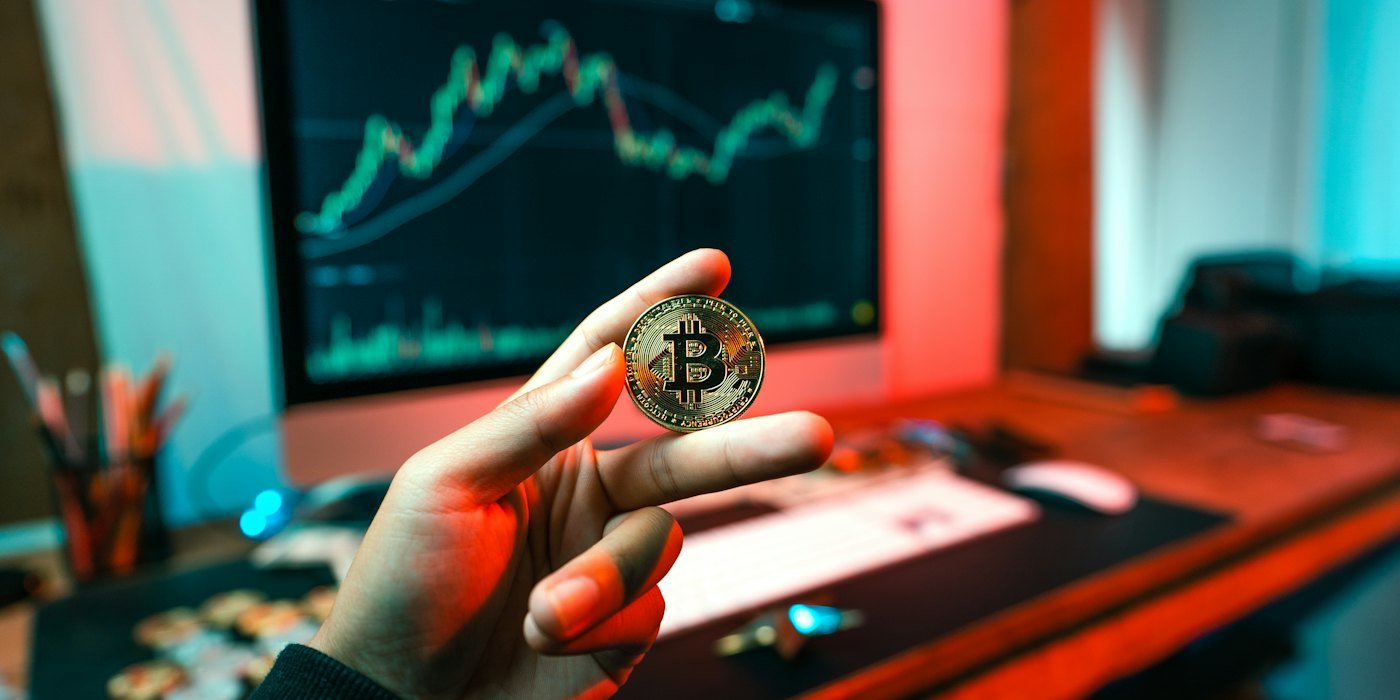 Una persona sosteniendo una moneda frente a una computadora — Cómo comprar un fondo indexado paso a paso