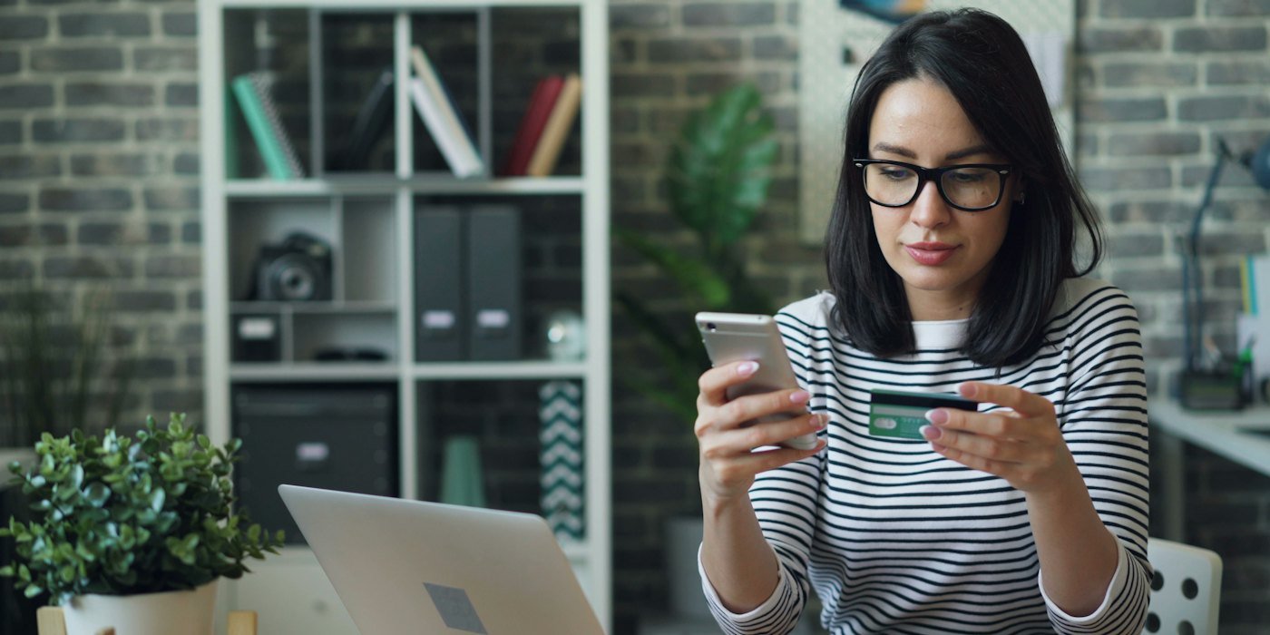 una mujer sentada en una mesa mirando su teléfono celular — Cómo negociar con tus acreedores