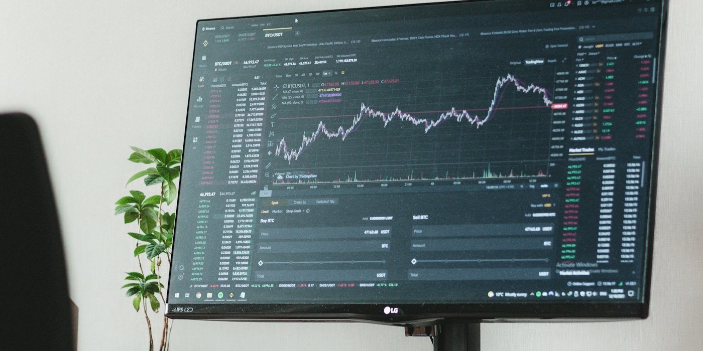 un monitor de computadora sentado encima de un escritorio de madera — Cómo seguir la actualidad financiera sin volverte loco
