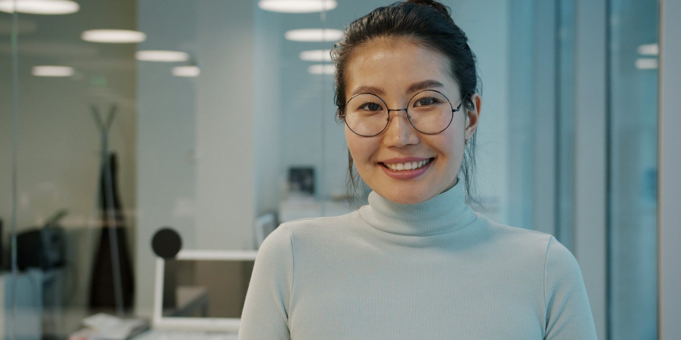 Una mujer sonriente con gafas en una oficina — Contrato formativo y de prácticas: derechos y condiciones