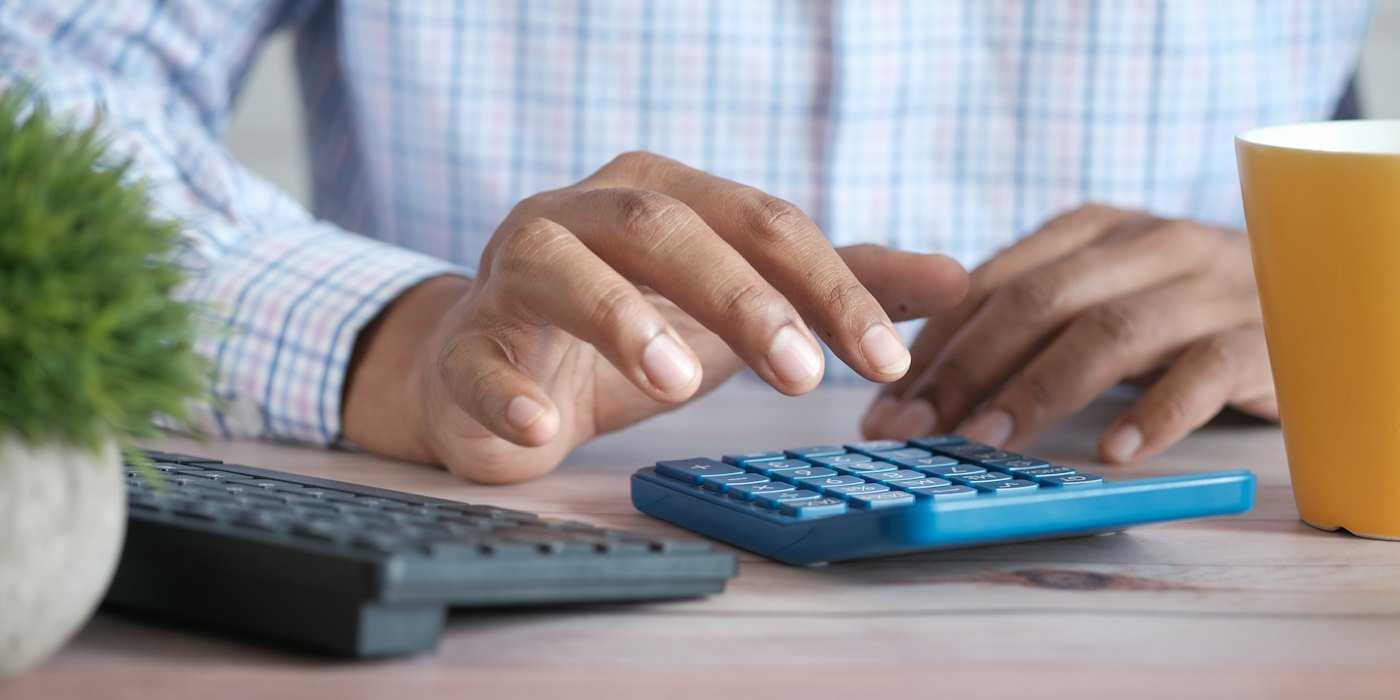 Persona usando la calculadora en el escritorio con una taza de café — Coste de oportunidad: cómo usarlo para decidir mejor