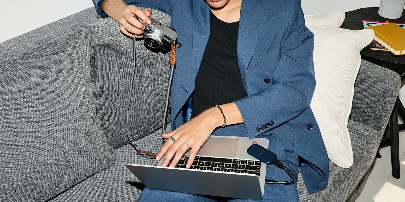 Joven usando portátil y cámara en el sofá — Cuánto cobrar como freelance: cómo calcular tu tarifa