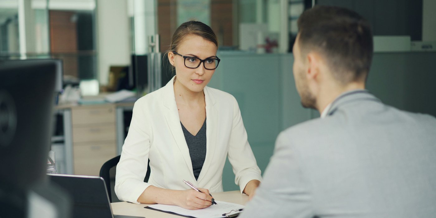 Mujer con gafas entrevista a un hombre en el escritorio de la oficina — Cuidar mascotas y casas como ingreso extra