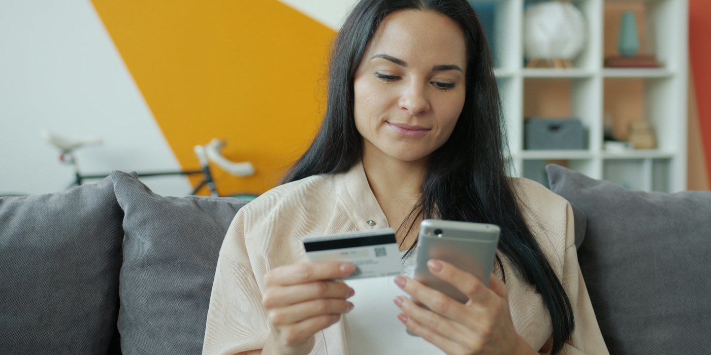Mujer sosteniendo tarjeta de crédito y teléfono para compras en línea — Financiar el móvil: cuánto pagas de más