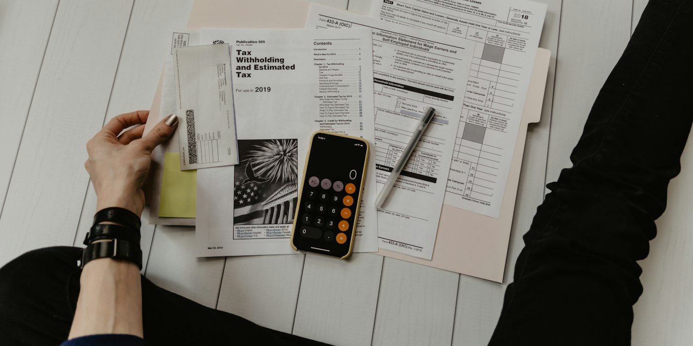 Persona sosteniendo papel cerca del bolígrafo y la calculadora — Finanzas personales desde cero: la guía completa para jóvenes