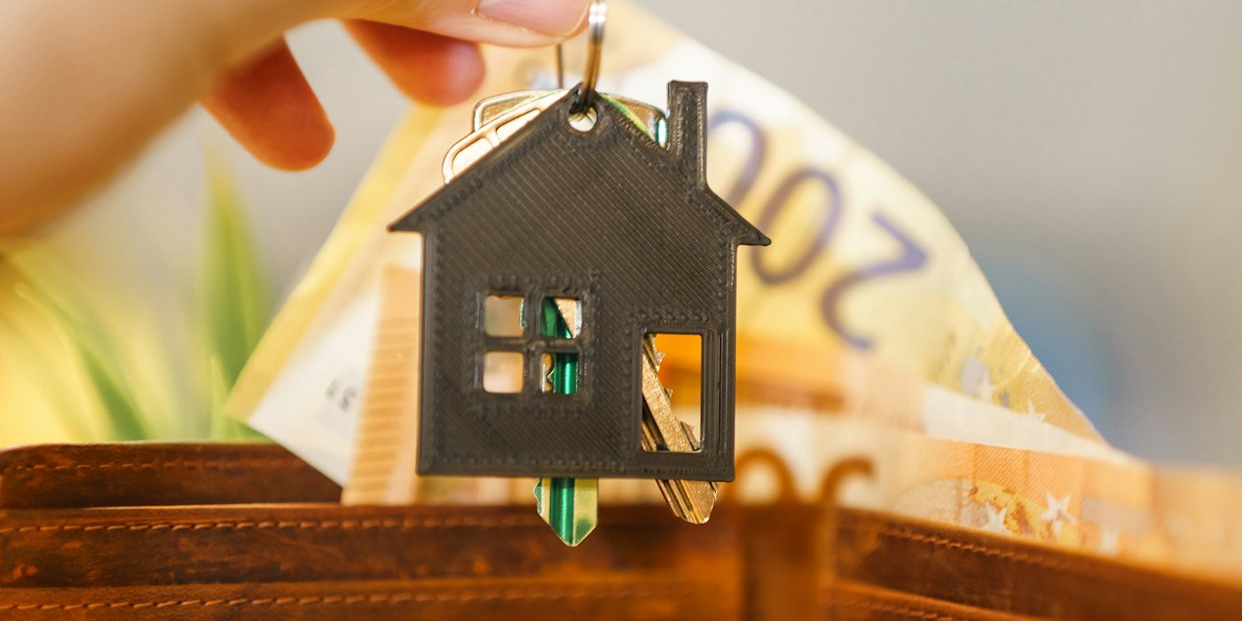 Una persona que pone la llave de una casa en una billetera — Gastos de compraventa de una vivienda