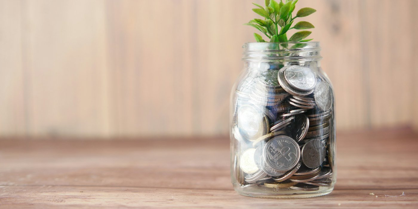 Un frasco de vidrio lleno de monedas y una planta — Herencias y donaciones: lo básico que debes saber