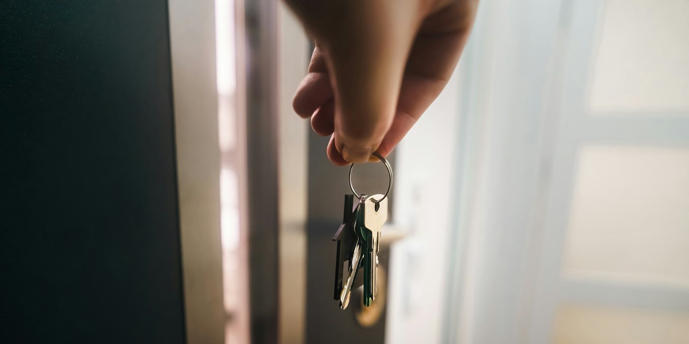 Una mano sostiene un llavero cerca de una puerta abierta — La tasación de una vivienda: qué es