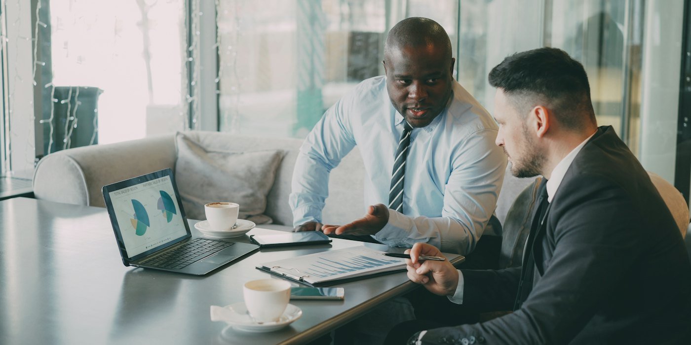 Dos hombres de negocios discutiendo gráficos en una computadora portátil — Planes de pensiones: ¿tienen sentido para un joven?