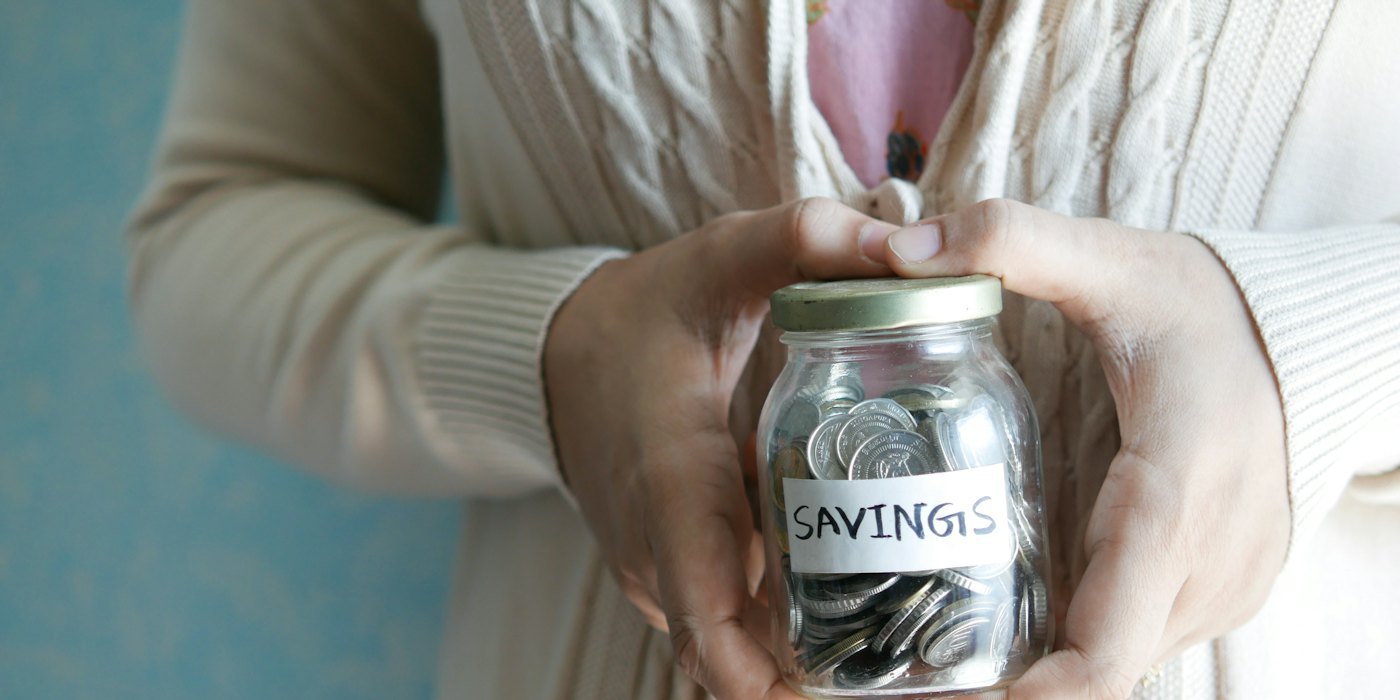 una mujer sosteniendo un frasco con ahorros escritos en él — Qué hacer con dinero inesperado