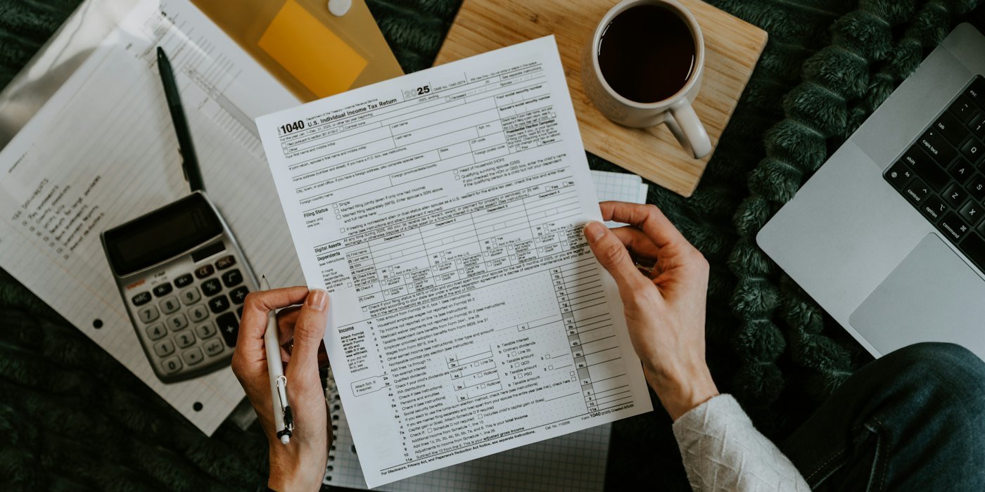 Manos sujetando formularios fiscales con calculadora y portátil — Seguro de vida, salud y hogar: cuándo merecen la pena