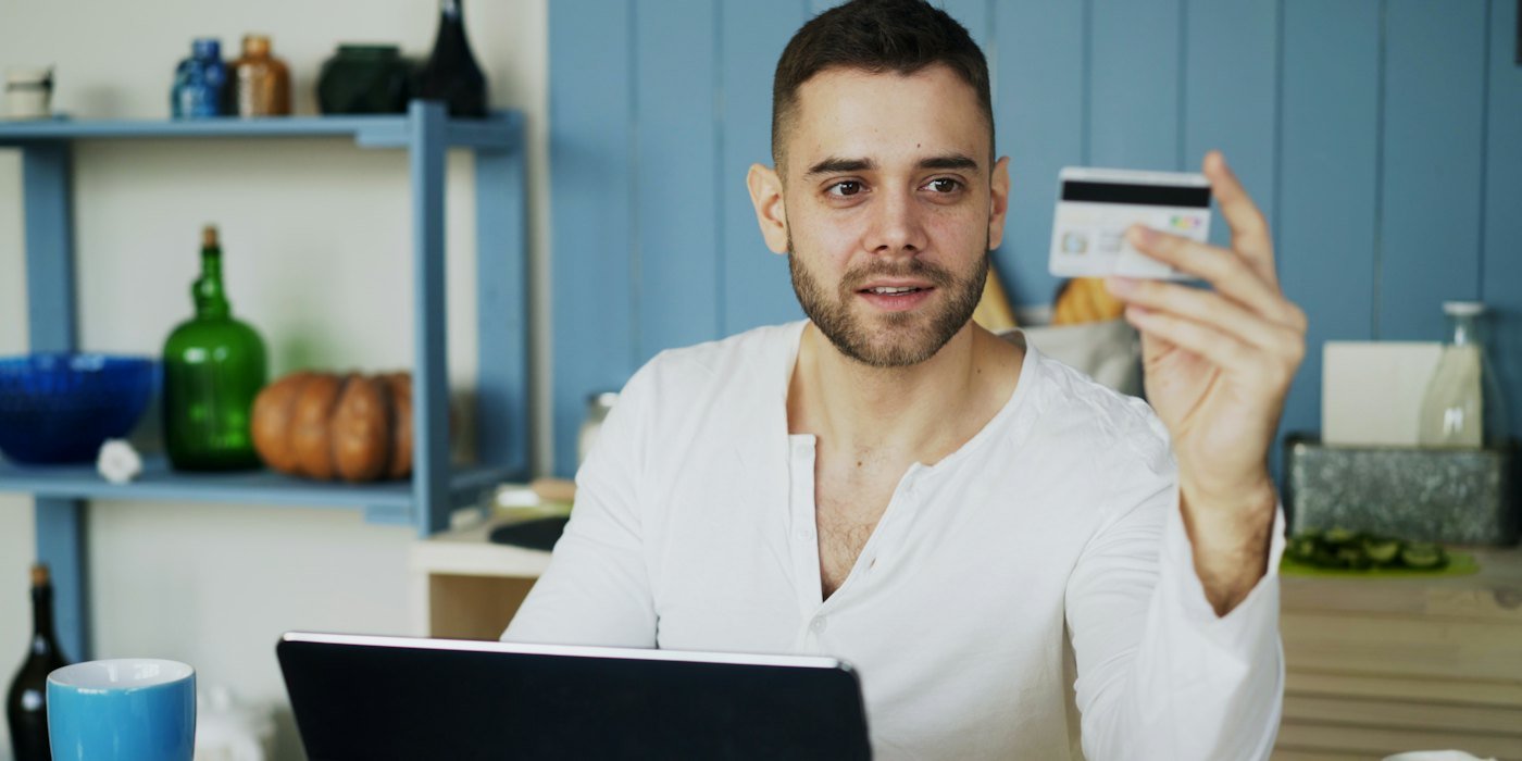 Hombre sosteniendo una tarjeta de crédito mientras mira una computadora portátil — TIN y TAE: qué significan de verdad