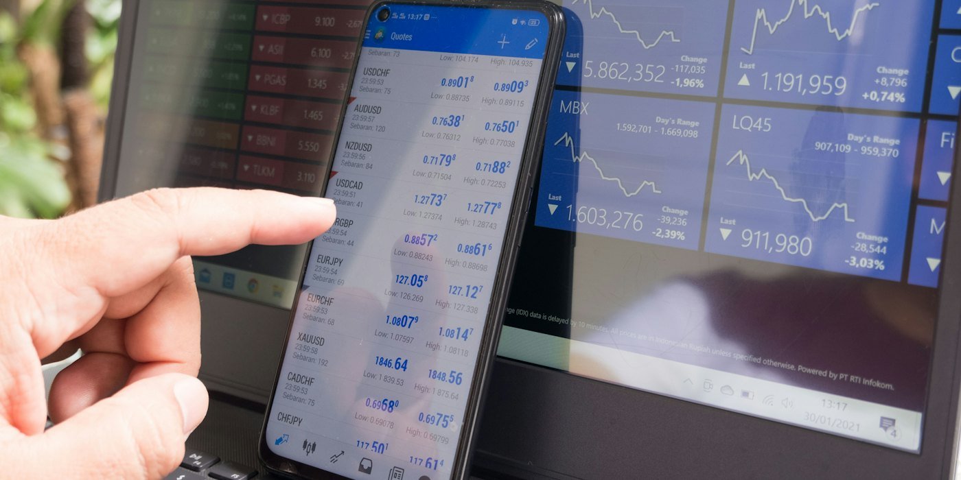 Una mano señalando un smartphone mostrando cotizaciones de divisas frente a un portátil — Volatilidad: cómo convivir con las caídas